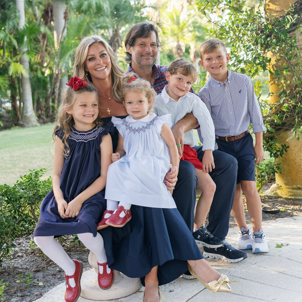 Family of six posing outdoors with palm trees in the background